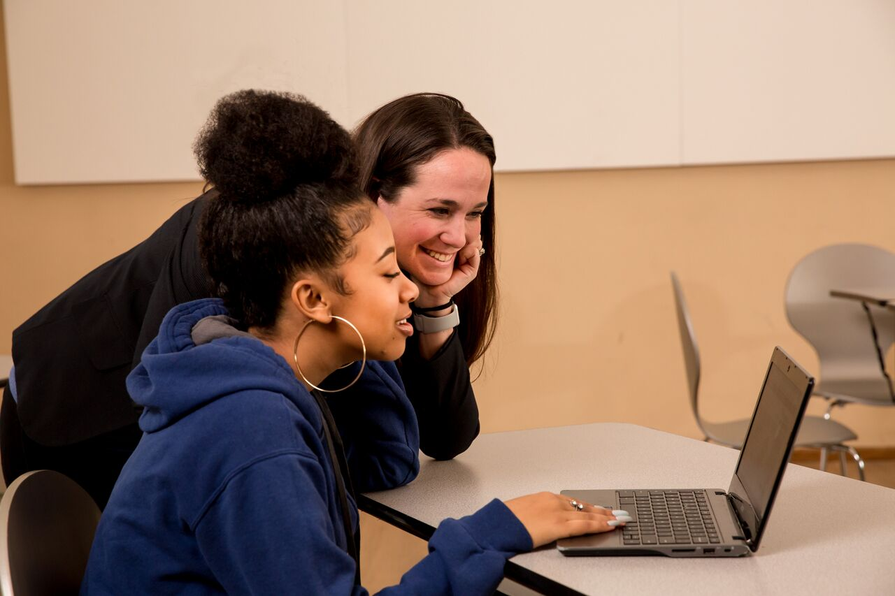 A teacher helping a student on her laptop.