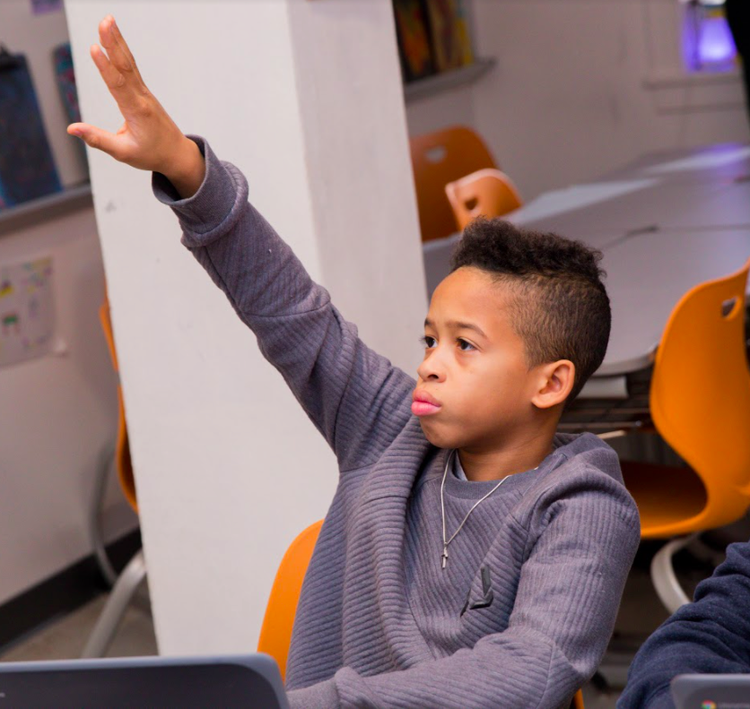 A student sitting and raising his hand. 