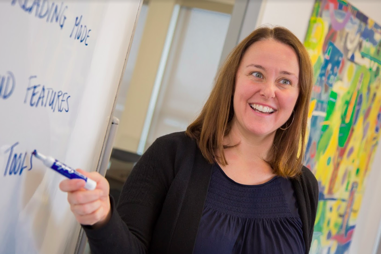 A teacher writing on the whiteboard and smiling.