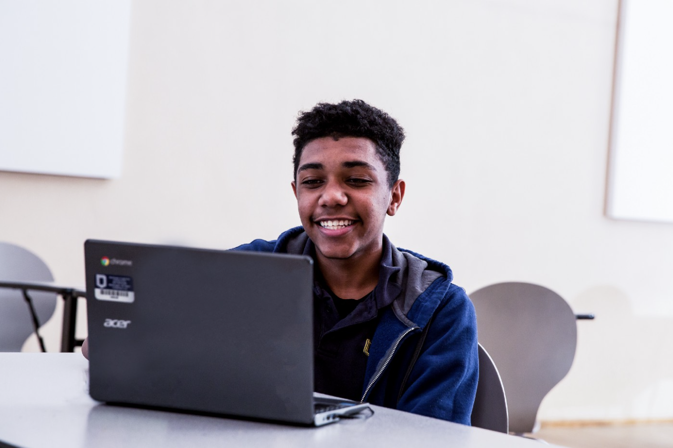 A student sitting at a table, looking at a computer screen, and smiling. 
