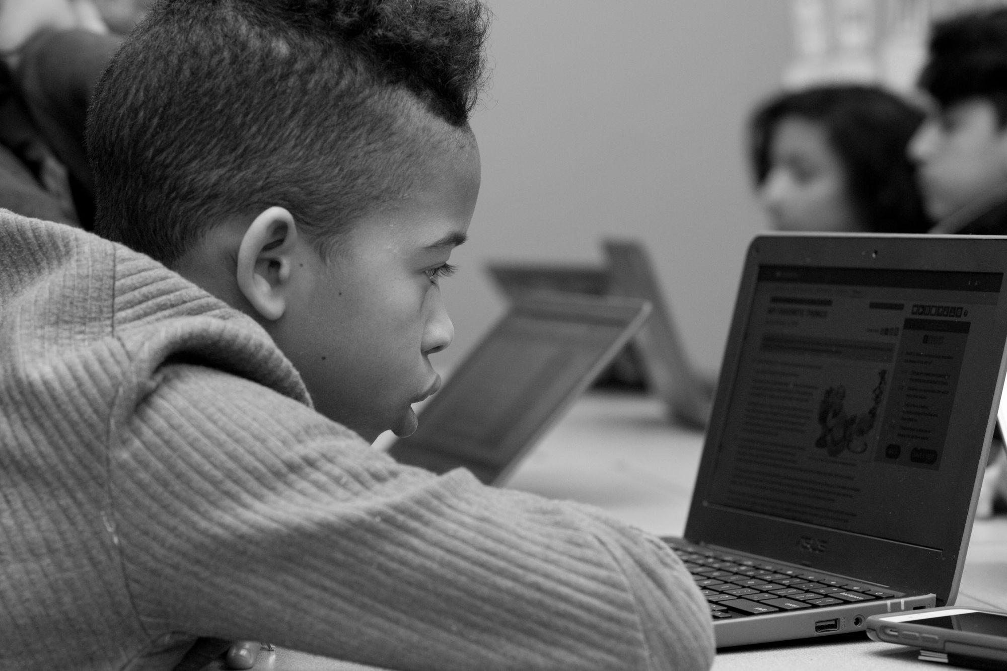 Black and white photo of boy looking at CommonLit lesson on laptop. 