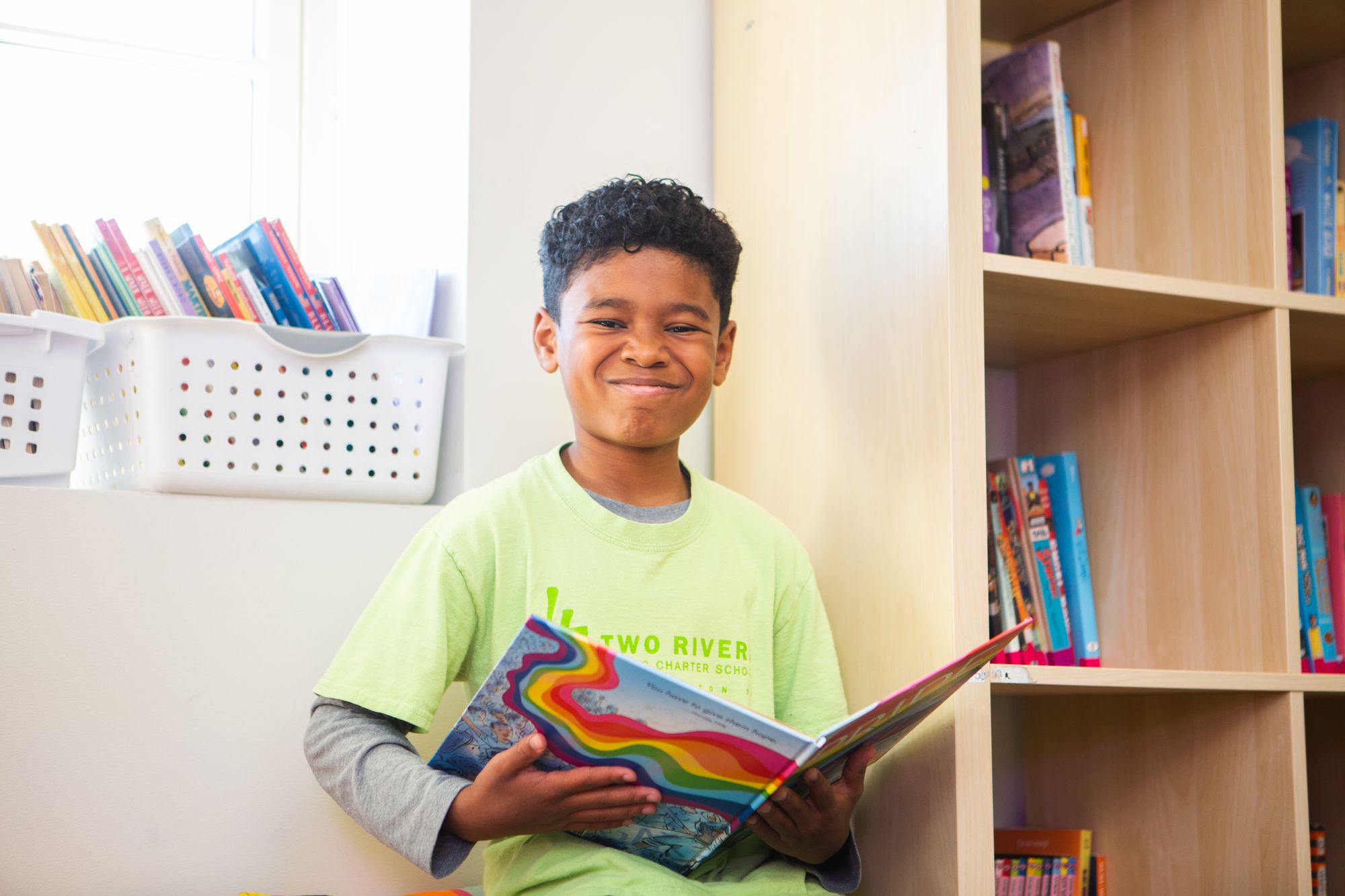 Boy smiles while reading a book with a colorful cover. 