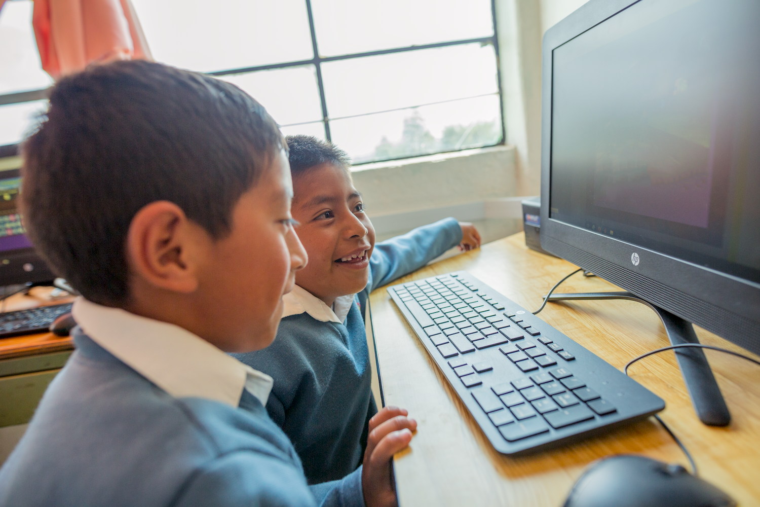 Two boy students look at CommonLit lesson on laptop. 