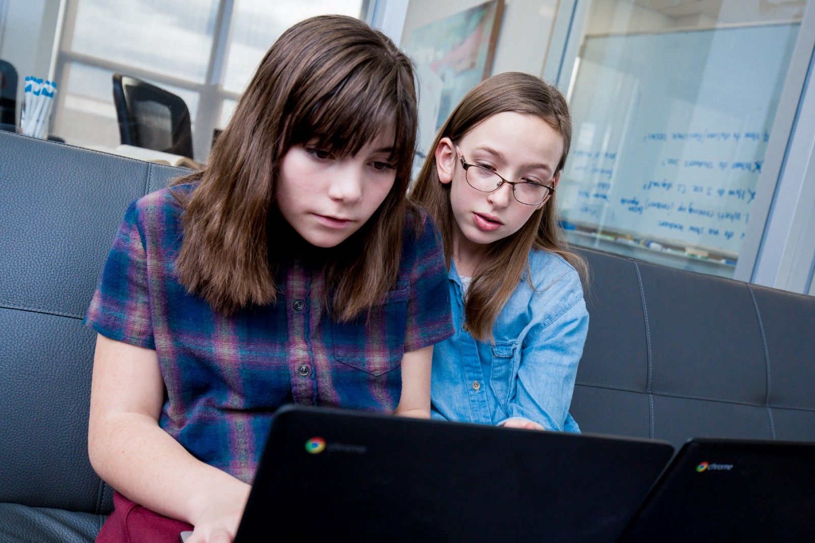 Two students sitting on a couch and looking at a computer screen. 