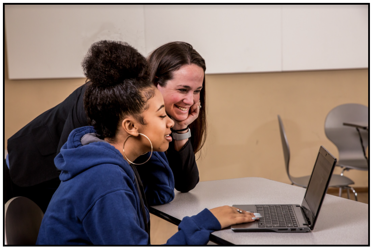 A teacher and student looking at a computer and smiling. 