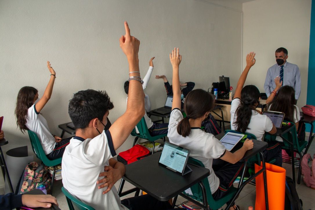 Estudiantes en una clase con sus manos levantadas por contestar una pregunta