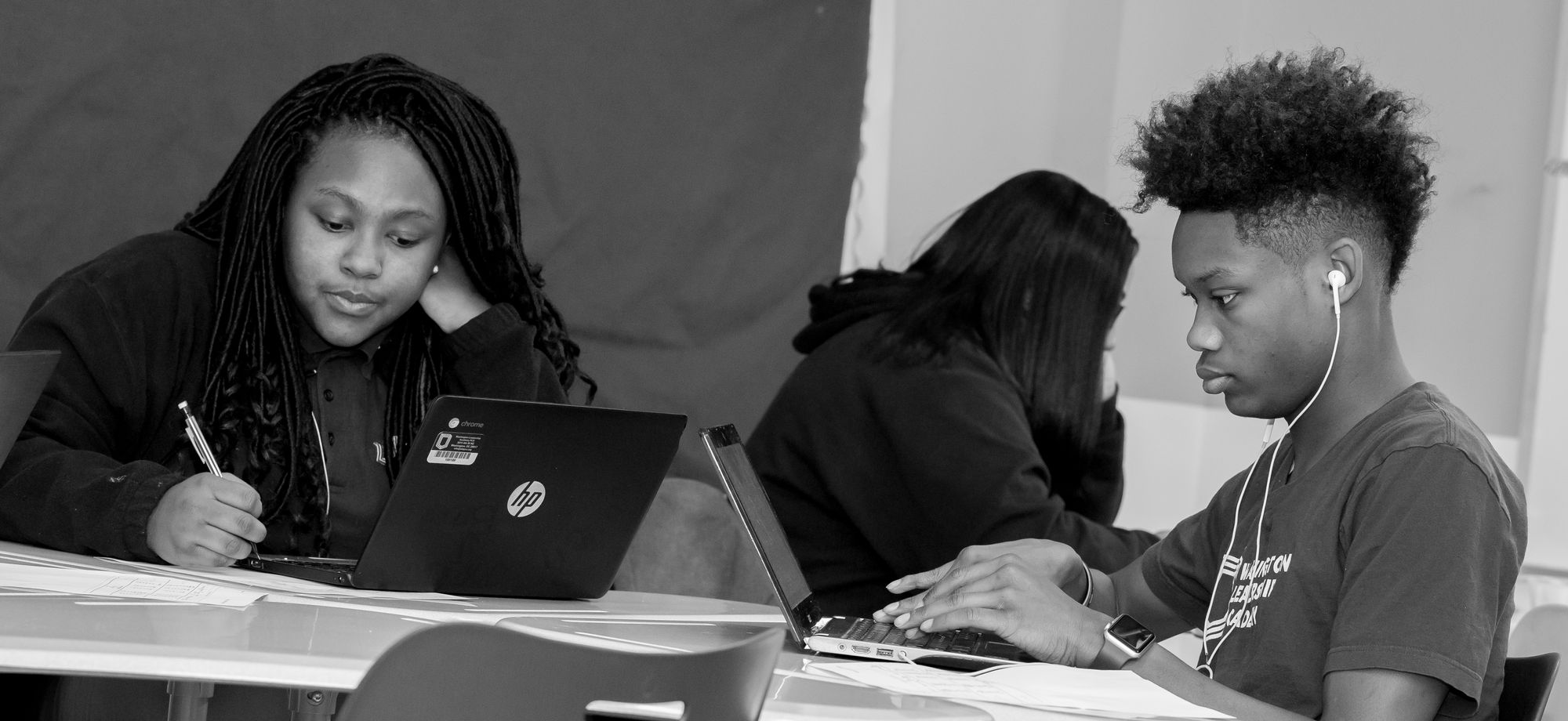 Black and white photo of two teenage students looking at CommonLit lesson on laptop. 