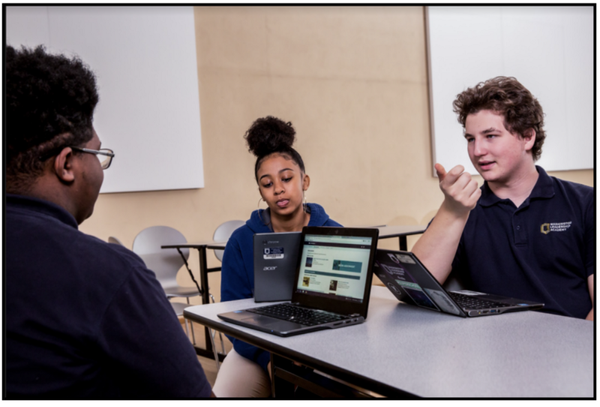 Three students sitting and talking to each other in front of their open computers. 