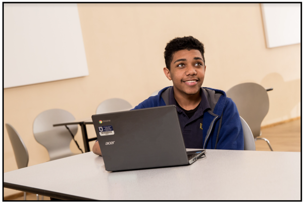 A student sitting at a table in front of a computer and looking up. 
