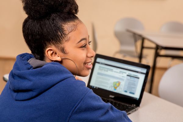 A student working on a CommonLit lesson on her computer and smiling. 