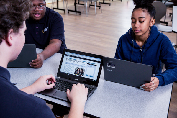 Three students sitting at a table and looking at their computer screens. 
