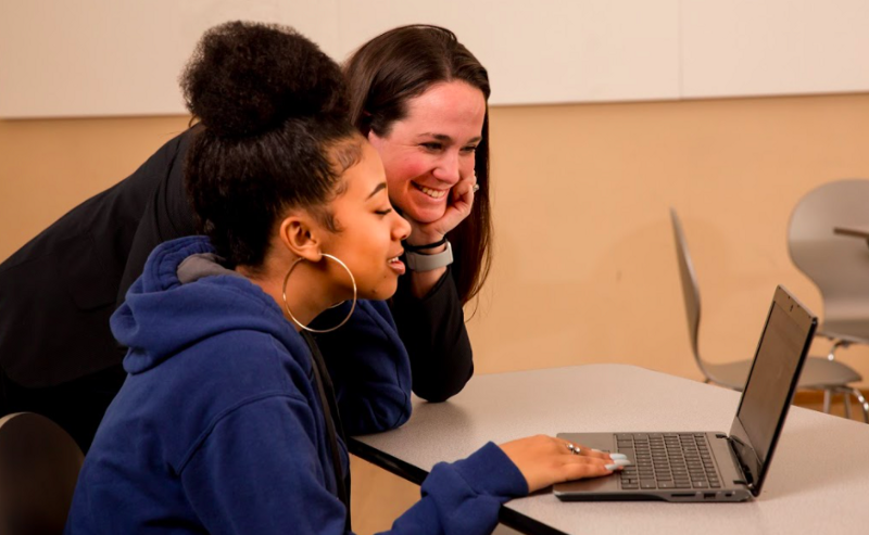 A teacher and a student look at a computer screen, smiling. 