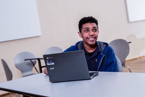 Teenage student smiles while looking up from laptop. 