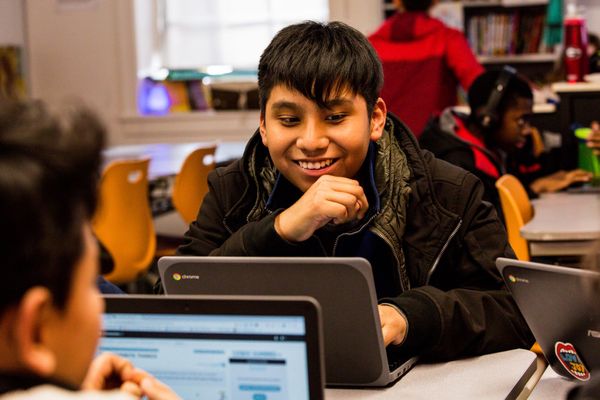 A student in the classroom smiles at his computer.