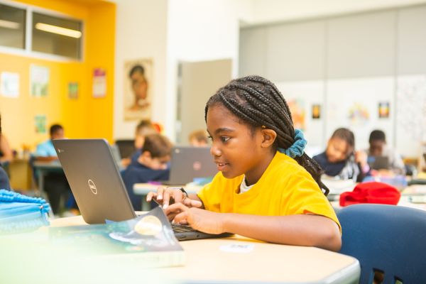 An elementary student works on a CommonLit Main Idea lesson. Other students in her class are visible in the background.